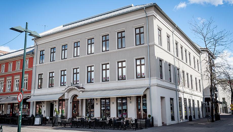 Lys bygård på hjørnet av et torg, med uteservering på gateplan