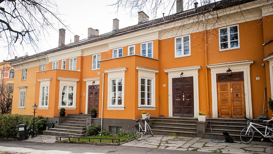 Okergul bygård med hvite vinduer og trapp opp til inngangen